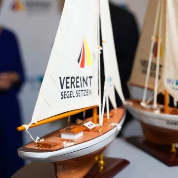 Das Modell eines Segelbootes, auf dessen Segel „vereint Segel setzen" steht.