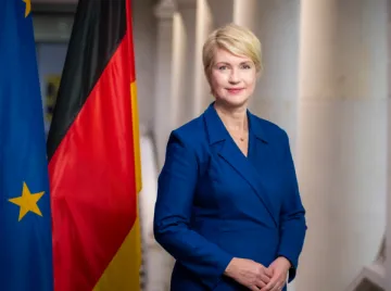 Eine Frau im blauen Kostüm. Am linken Bildrand eine Europafahne und eine Deutschlandfahne.
